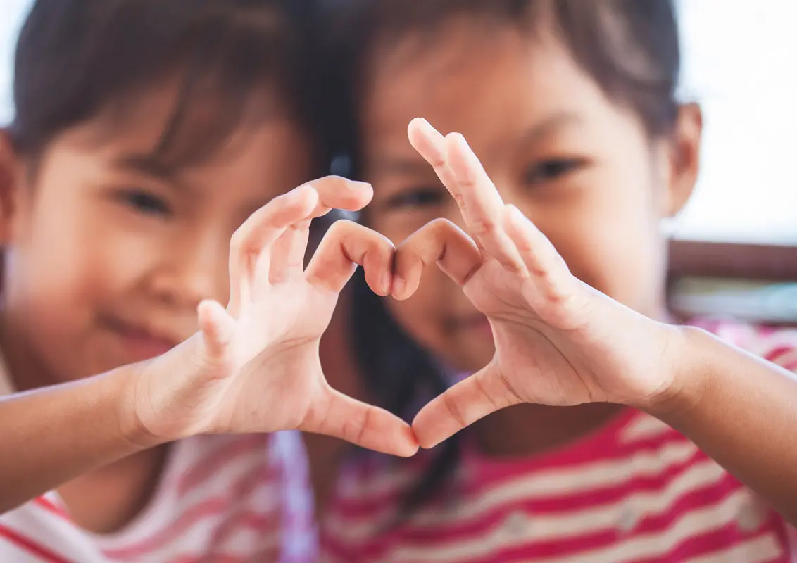 Two kids using their hands to make a heart